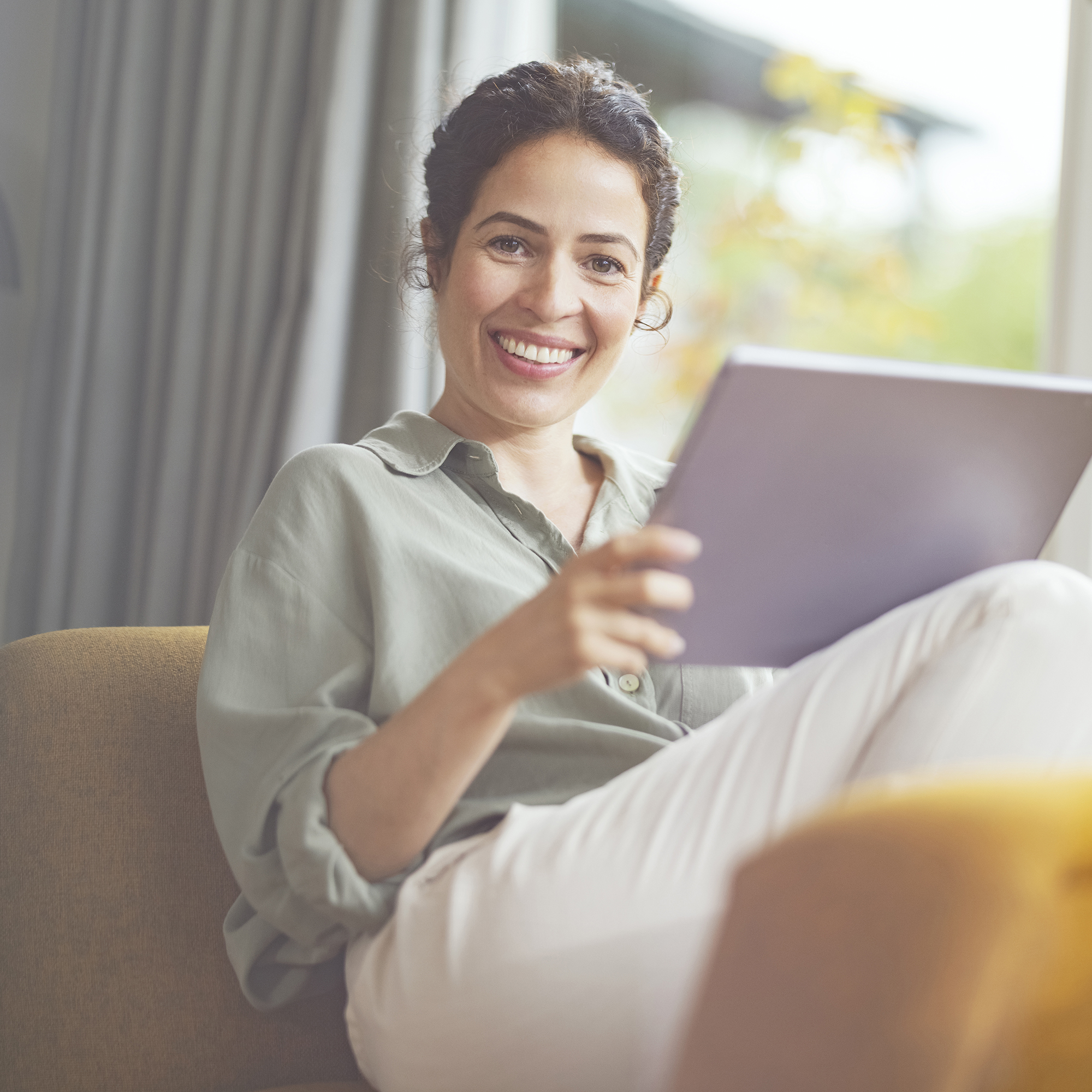 Lachende Frau mit Tablet auf dem Sofa